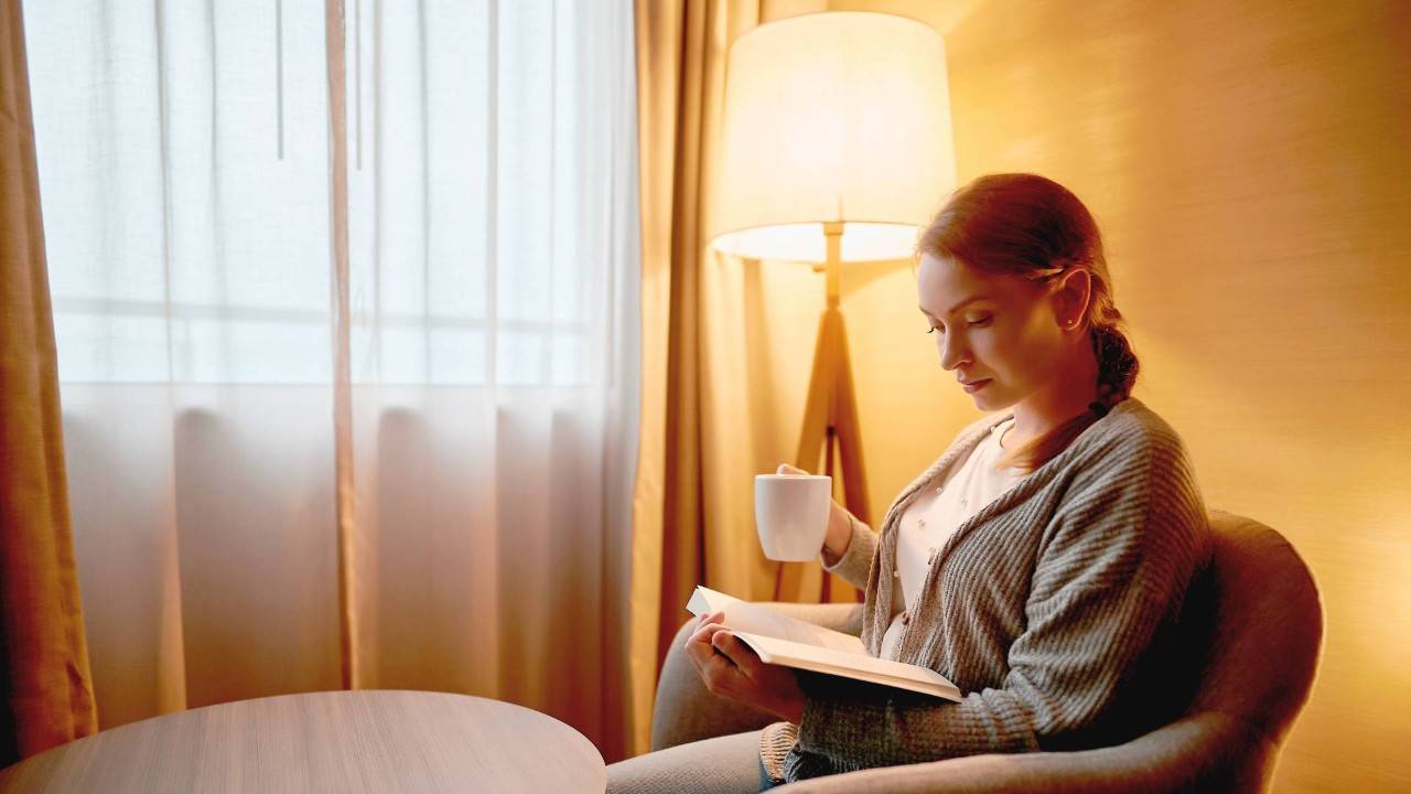 Joven leyendo bajo lámpara en casa