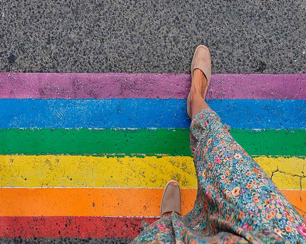 A person on a crosswalk with the colors of the LGBTQI+ flag